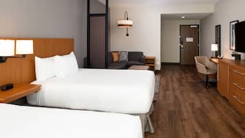 A hotel room with two beds, a desk, a chair, a TV, and a lamp.