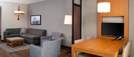 Una sala de estar moderna con un sofá gris, un sillón azul, una mesa de comedor de madera y un televisor de pantalla plana montado en la pared.