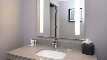 A modern bathroom with a marble sink, a large mirror, and a framed artwork on the wall.