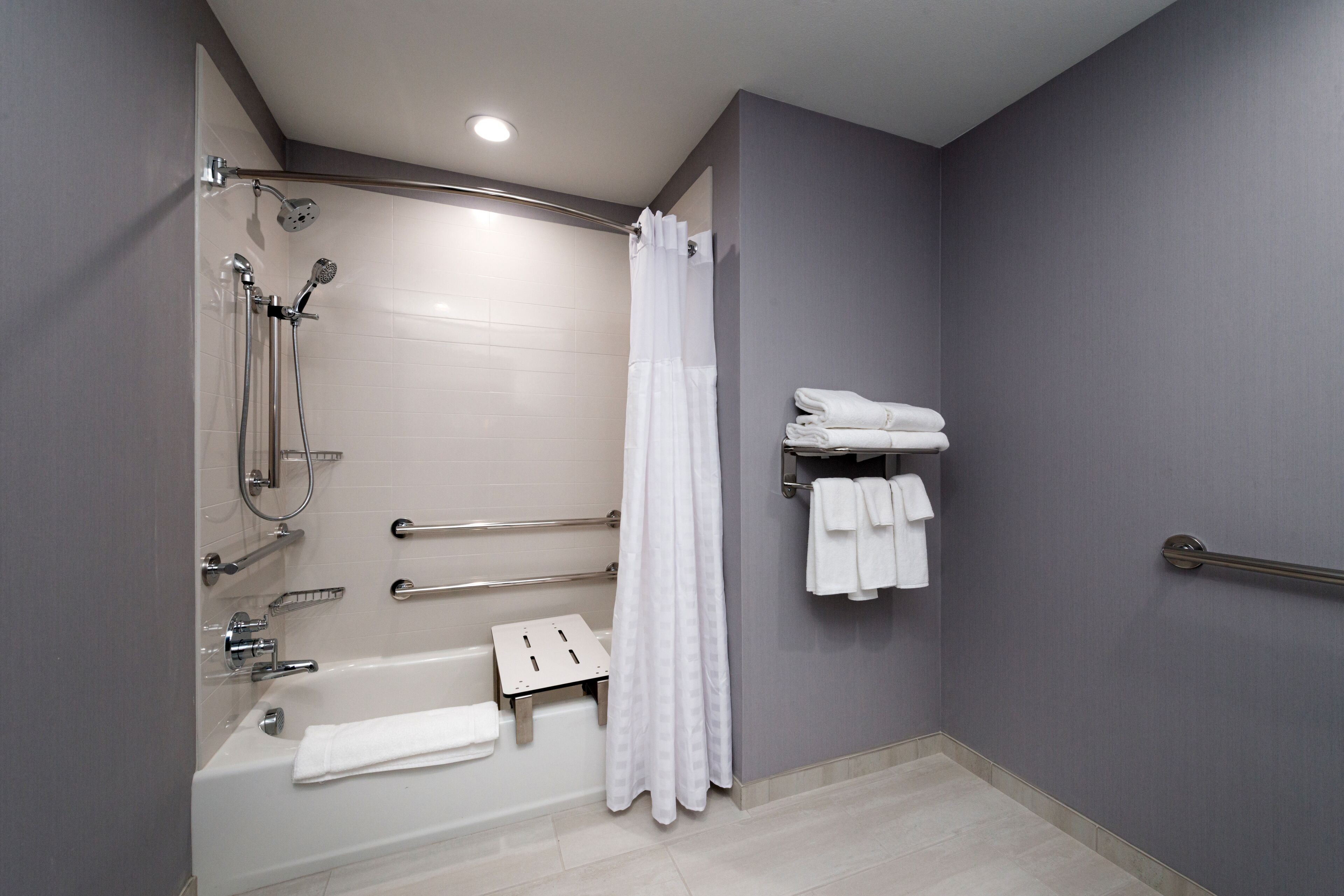A modern bathroom with a walk-in shower, grab bars, a white bathtub, and a towel rack.