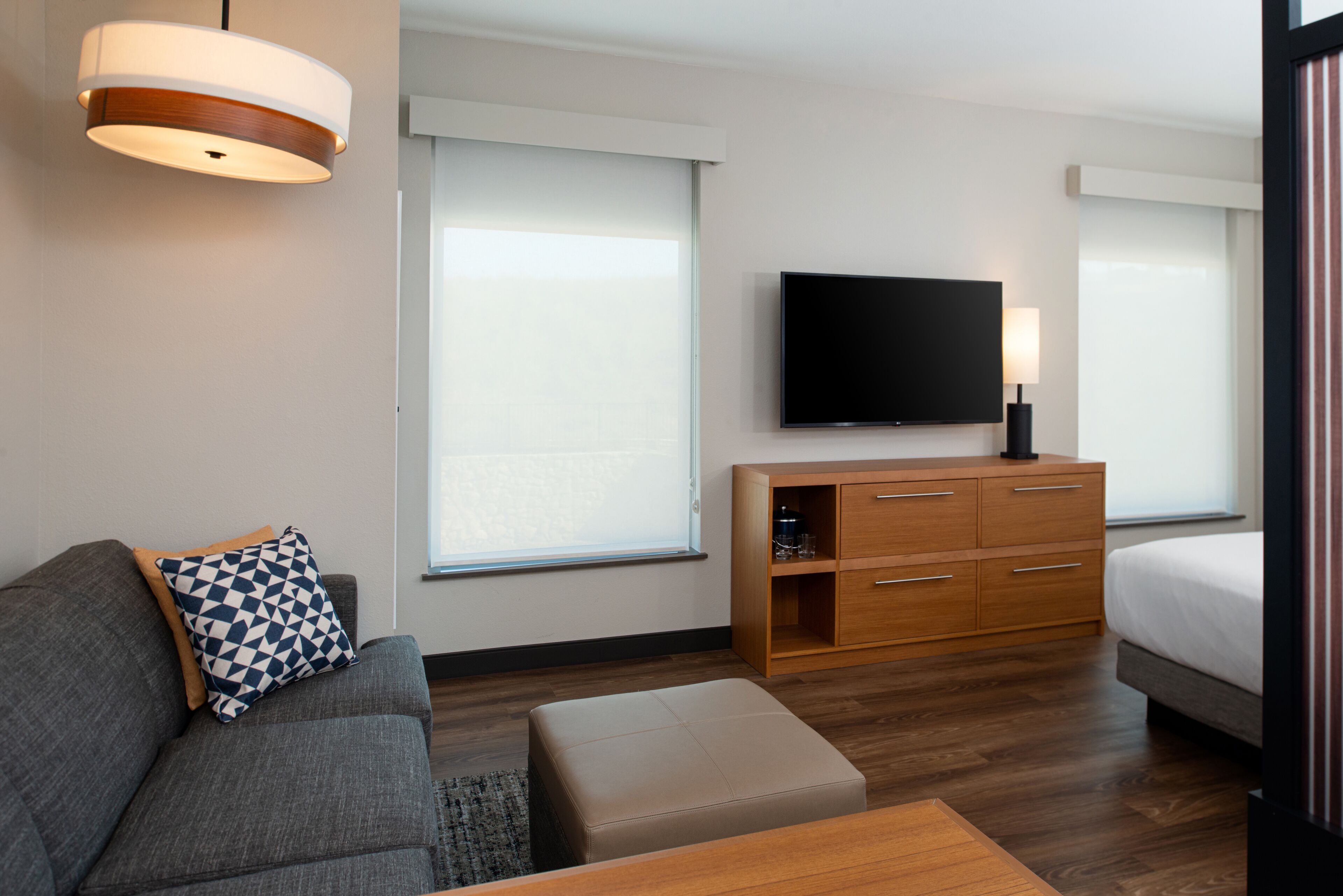 Quarto de hotel moderno com sofá cinzento, armário de madeira, televisão de ecrã plano e uma cama.
