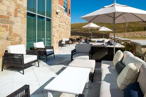 An outdoor patio with stone walls, wicker furniture, and white cushions.