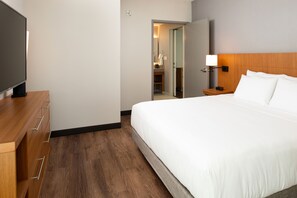 A hotel room with a bed, a TV, a wooden dresser, and a nightstand with a lamp. - Hyatt Place Dallas/Rockwall (Rockwall)