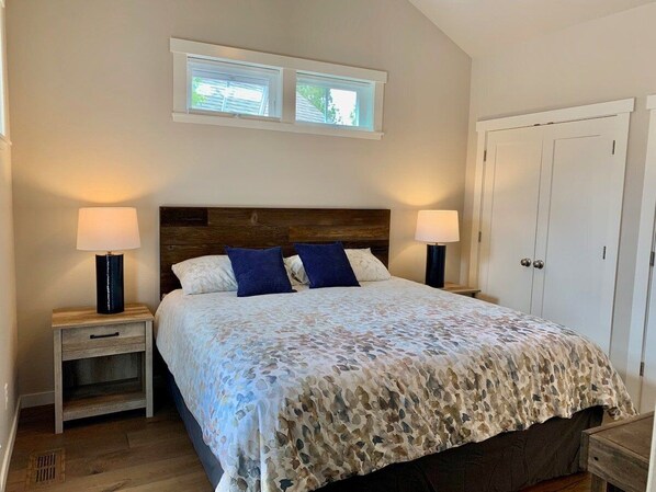 A bedroom with a bed, two nightstands, two lamps, a wooden headboard, a window, and a door. - Bluebird Day - River Trail House, Enjoy a cozy retreat in Bend, OR. (Bend)