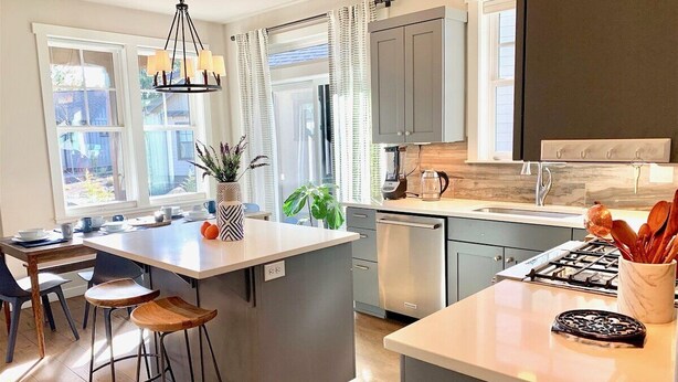 A modern kitchen with a central island, bar stools, and a dining area with a table and chairs. - Bluebird Day - River Trail House, Enjoy a cozy retreat in Bend, OR. (Bend)