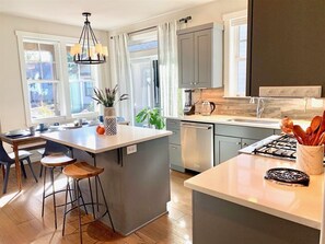 A modern kitchen with a central island, bar stools, and a dining area with a table and chairs. - Bluebird Day - River Trail House, Enjoy a cozy retreat in Bend, OR. (Bend)
