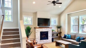 A spacious living room with a fireplace, a sofa set, a coffee table, and a TV mounted above the fireplace. - Bluebird Day - River Trail House, Enjoy a cozy retreat in Bend, OR. (Bend)