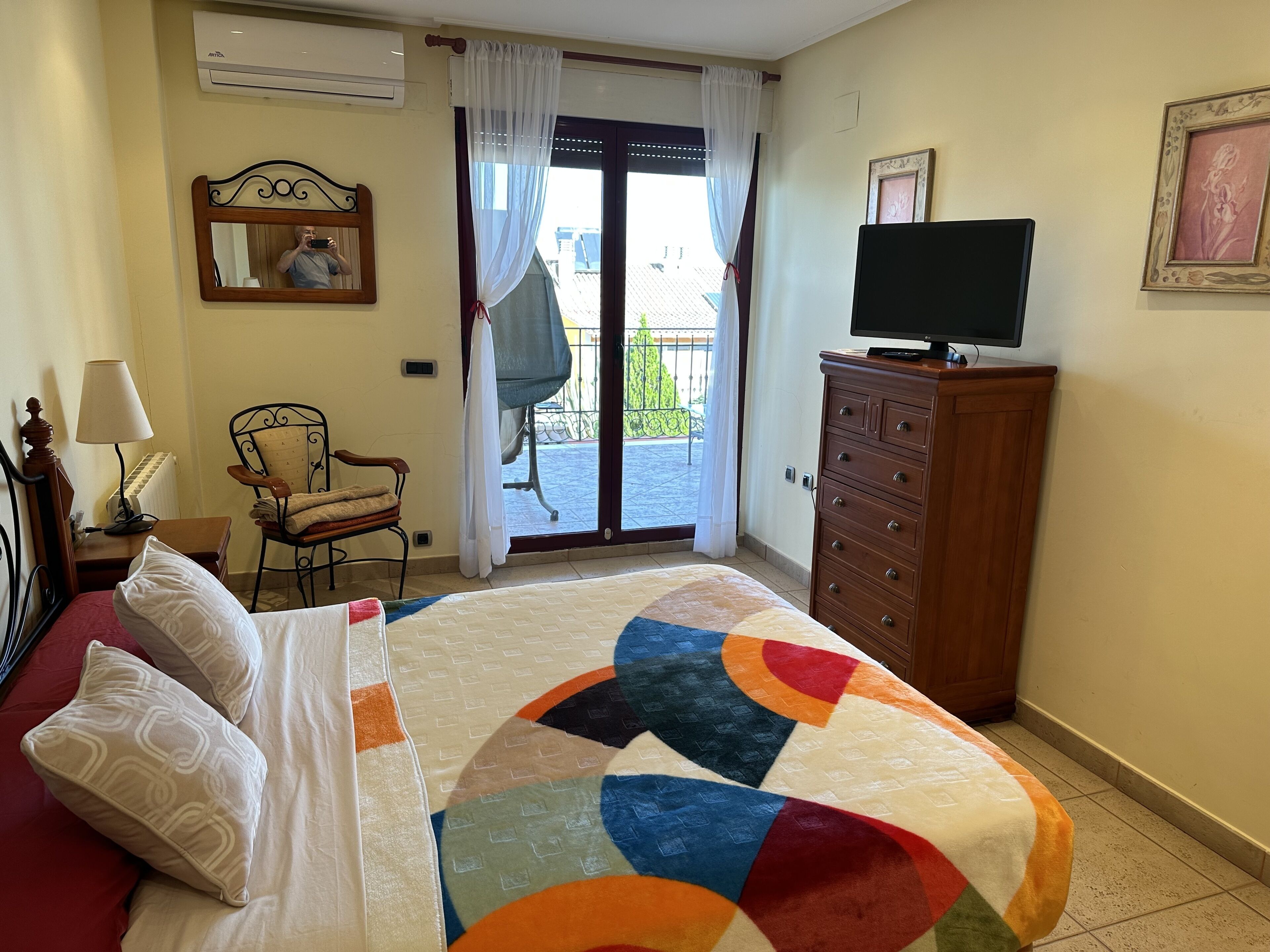 Une chambre d’hôtel avec un lit, un téléviseur posé sur une commode en bois, une chaise et un balcon avec vue.