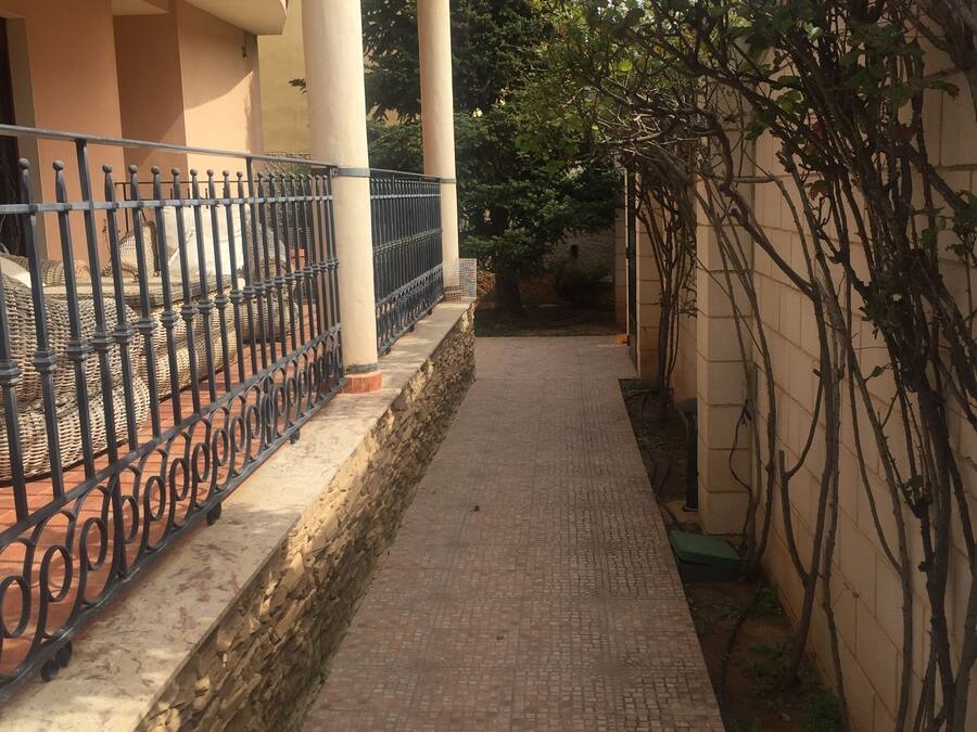 A covered walkway with a brick floor, bordered by a stone wall and a metal fence.