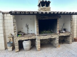Una cocina al aire libre de piedra con salpicadero de azulejos, una gran urna de piedra y una pequeña mesa de madera.