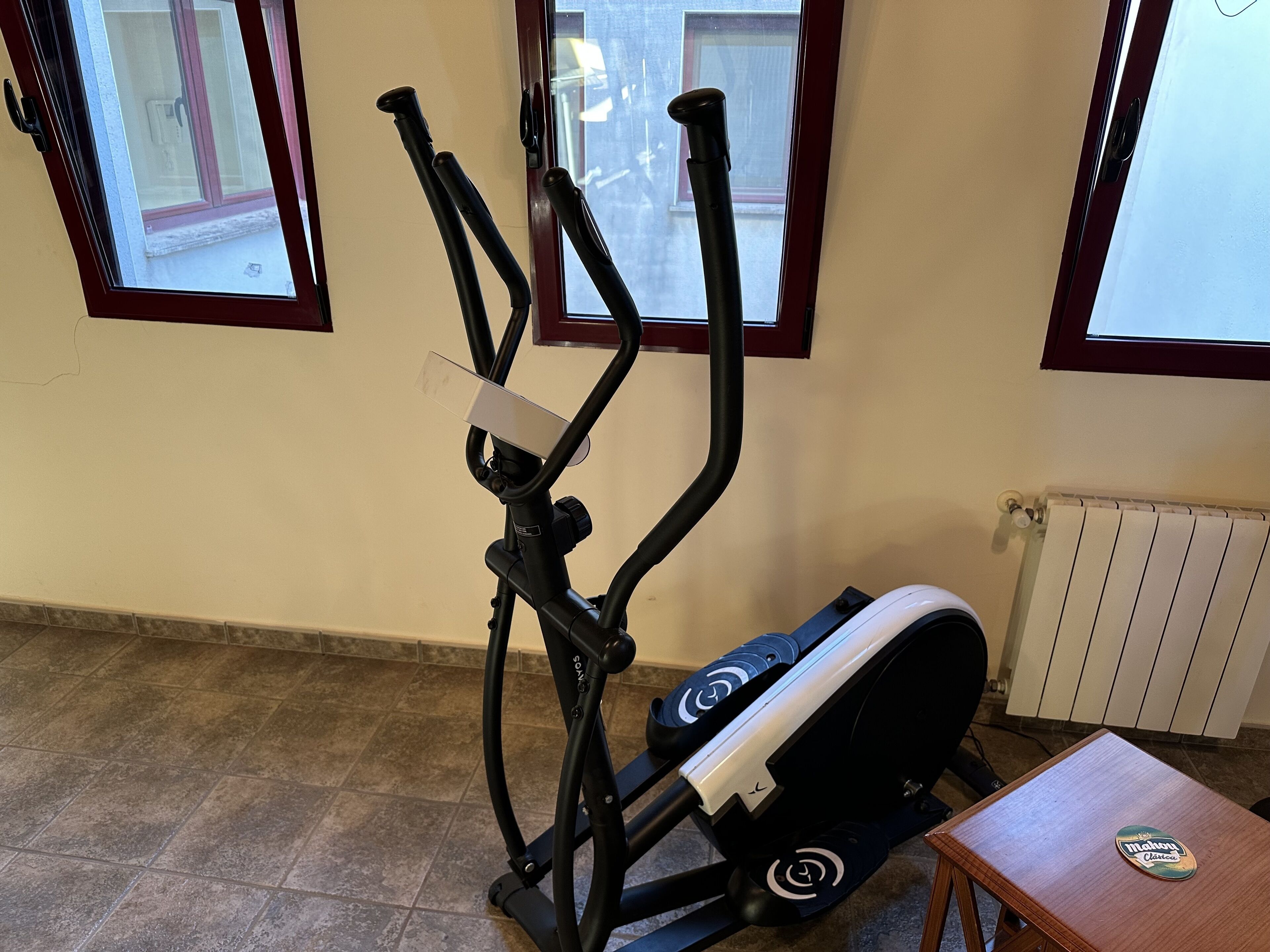 Een fitnessapparaat in een ruimte met betegelde vloer, een radiator en een raam met uitzicht.