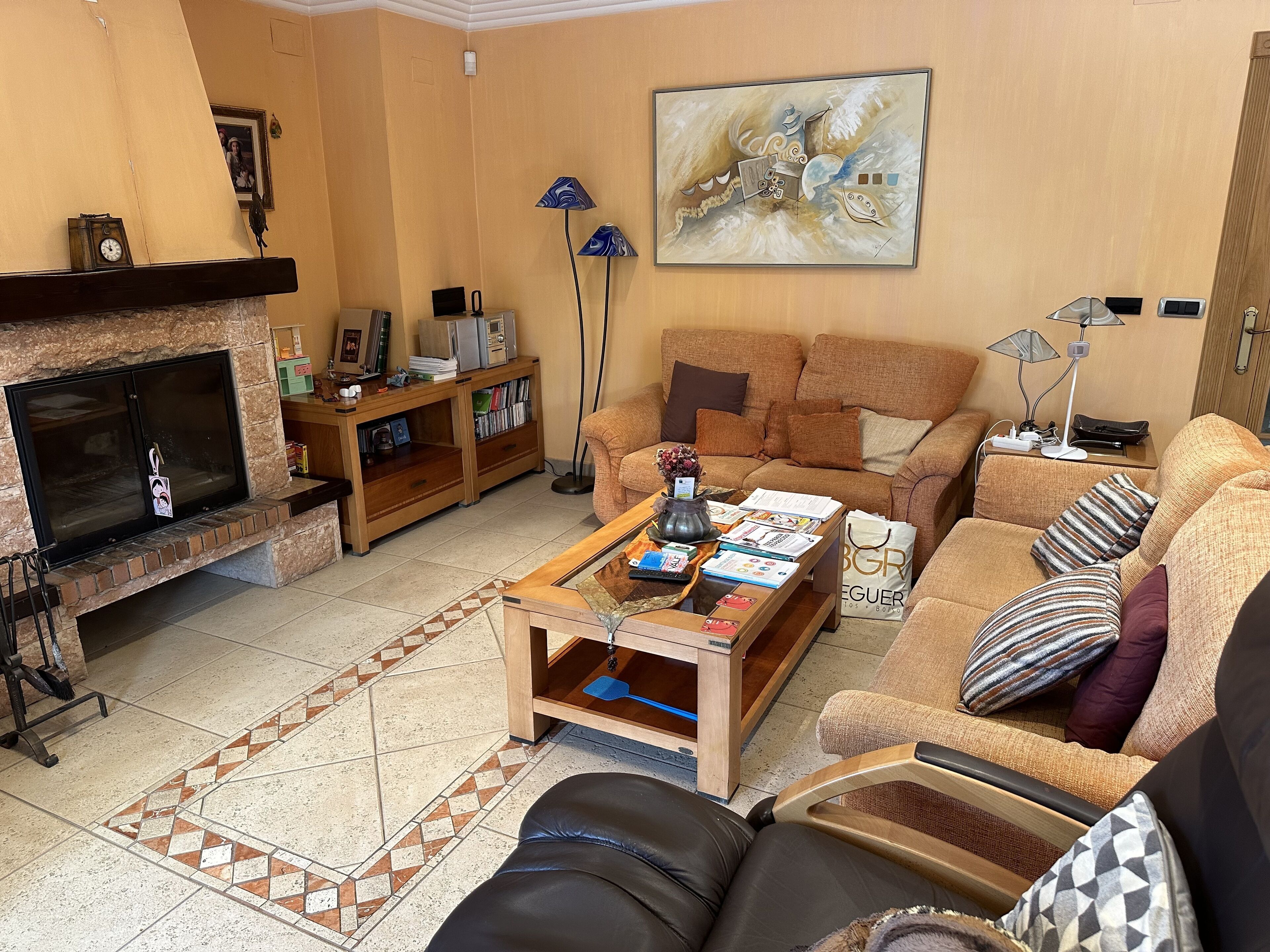 A living room with a fireplace, sofa, coffee table, and a painting on the wall.