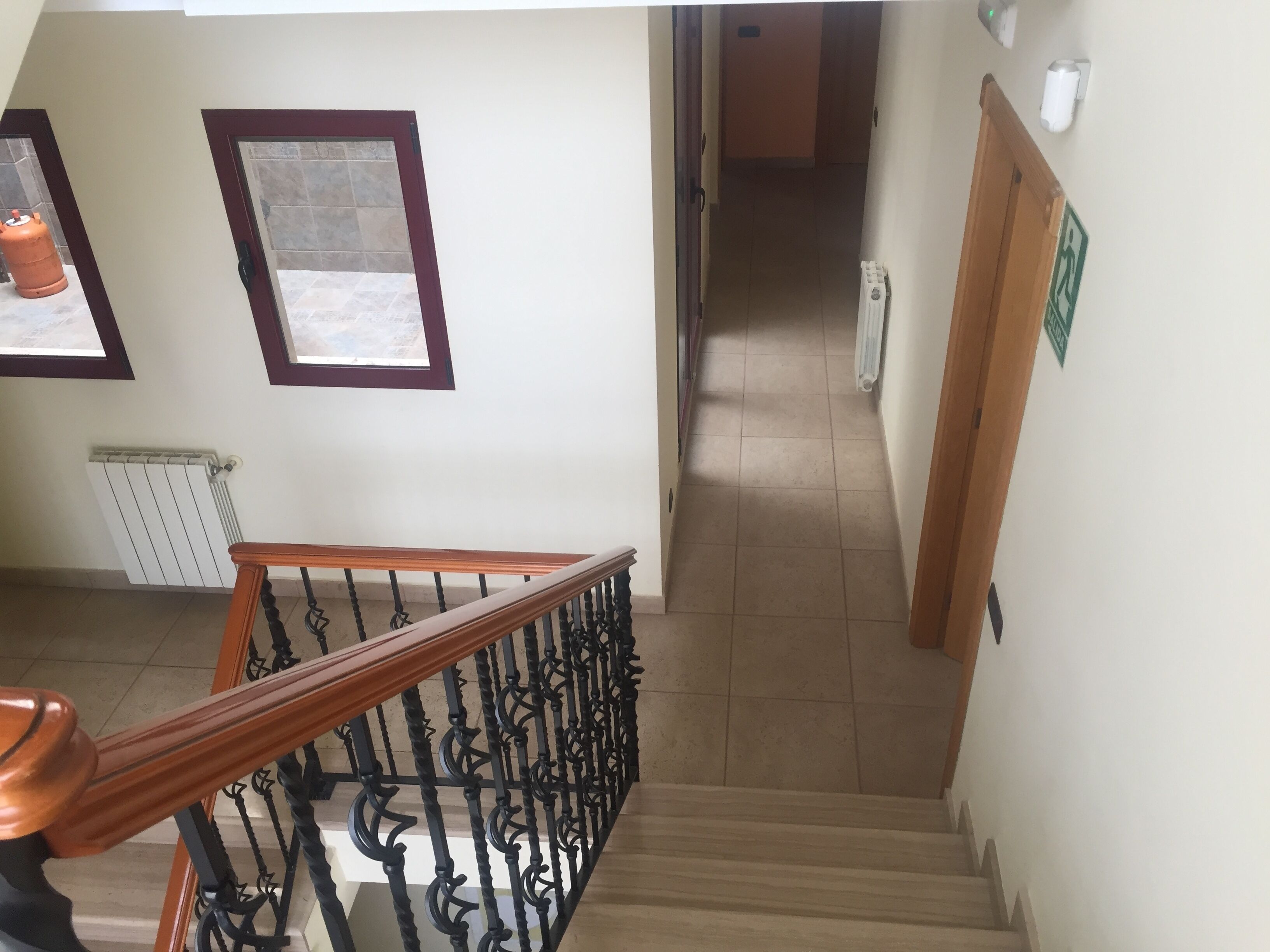 A staircase with a wooden handrail and black balusters, leading to a hallway with a radiator and a fire extinguisher on the wall.