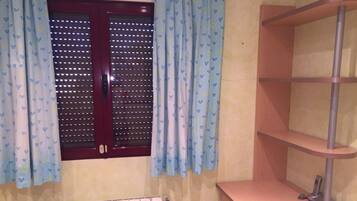 A bathroom with a window, a radiator, a wooden shelf, and a mirror.
