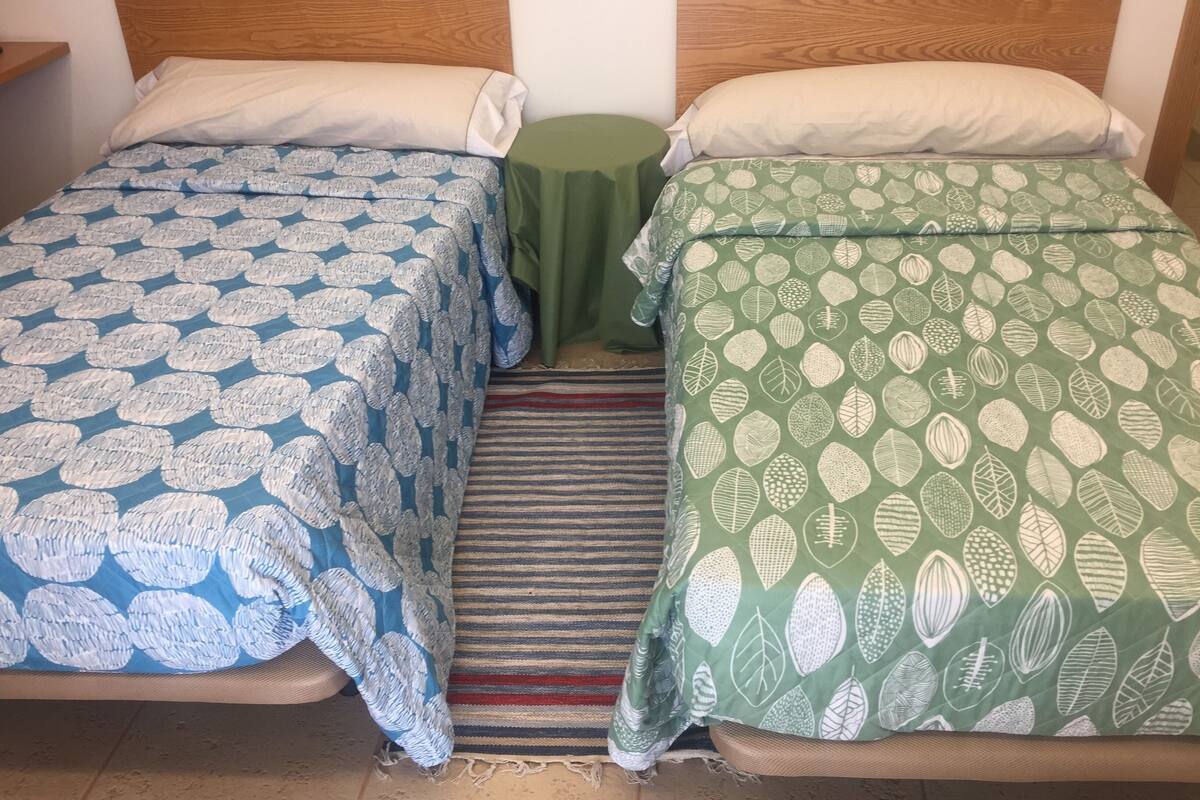 Two single beds with wooden headboards, a green table between them, and a striped rug on the floor.