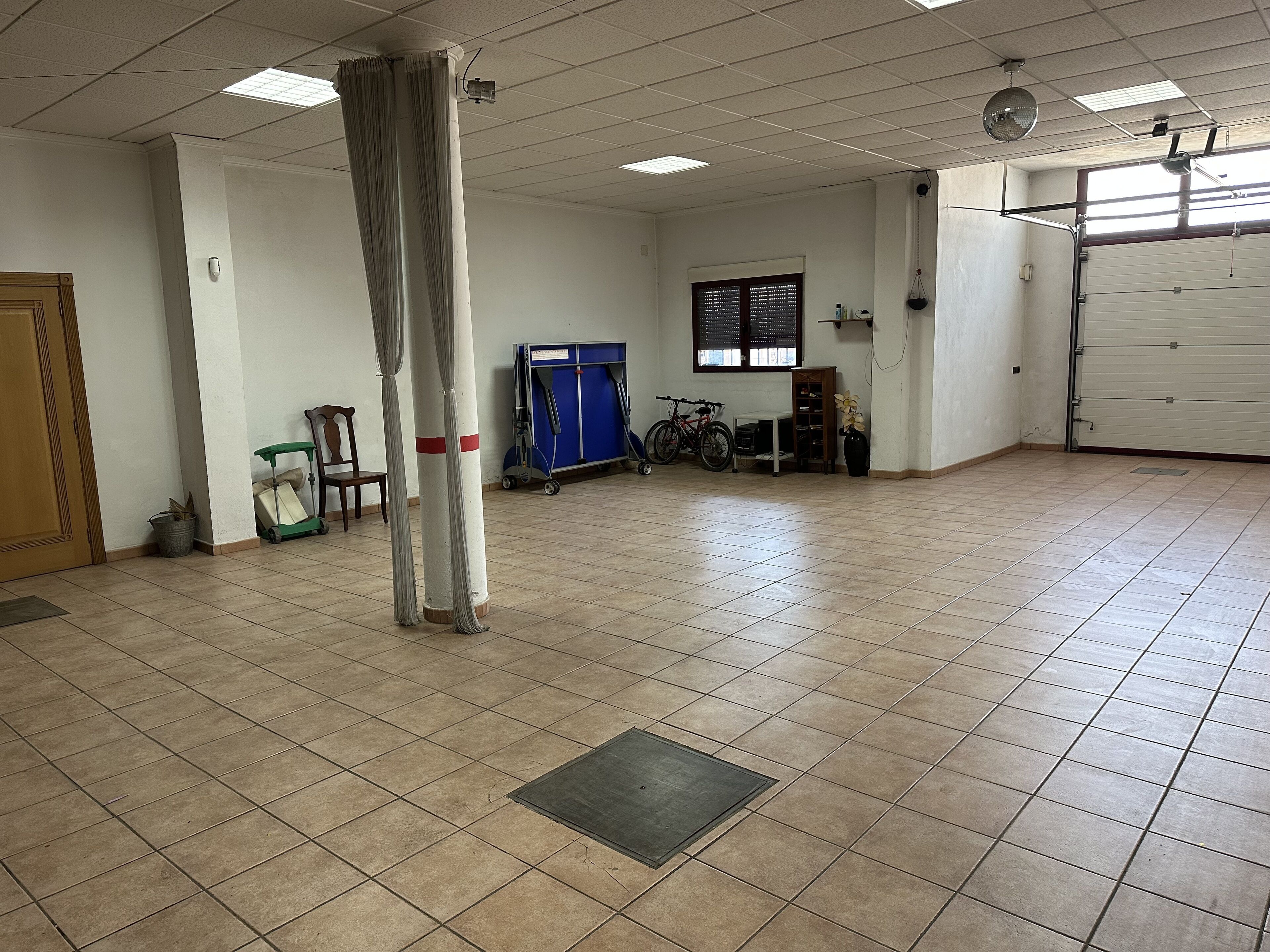 A spacious room with tiled flooring, a large pillar, a bicycle, and a window with blinds.