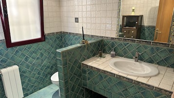 Une salle de bain avec un lavabo blanc, des carreaux verts à motifs, des toilettes et un miroir avec un cadre en bois.