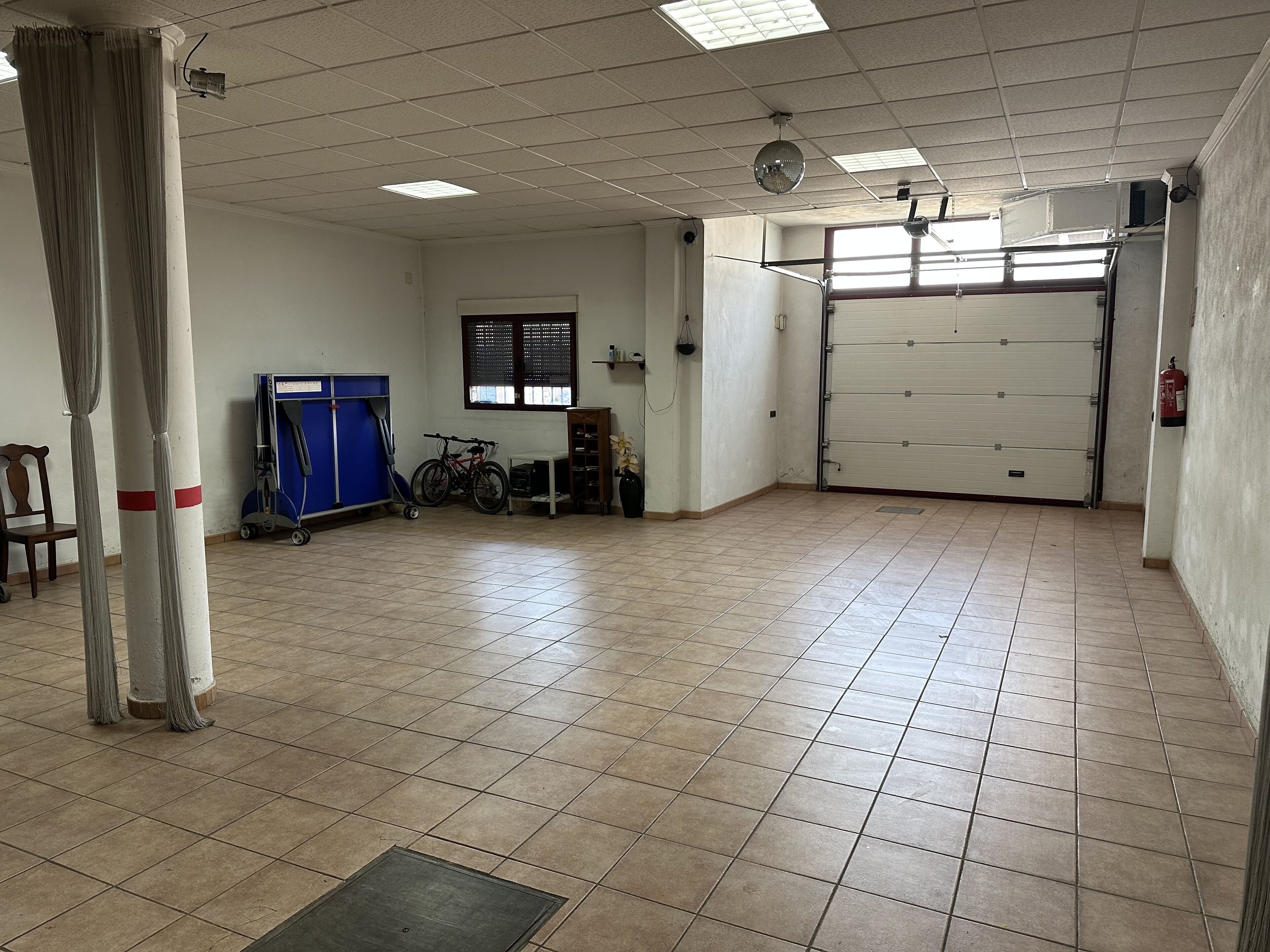 Una habitación amplia con suelo de baldosas, un ventanal grande, una puerta de garaje cerrada y una bicicleta.