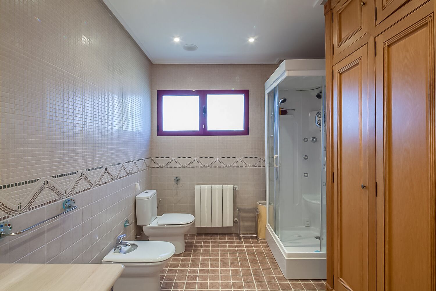 A bathroom with a shower, two toilets, a sink, and a window.