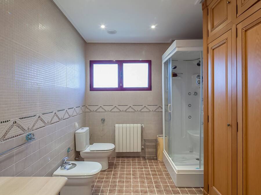 A bathroom with a shower, two toilets, a sink, and a window.