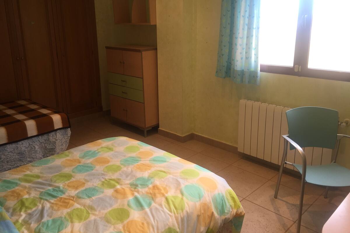 A bedroom with a bed, a dresser, a chair, and a window with curtains.