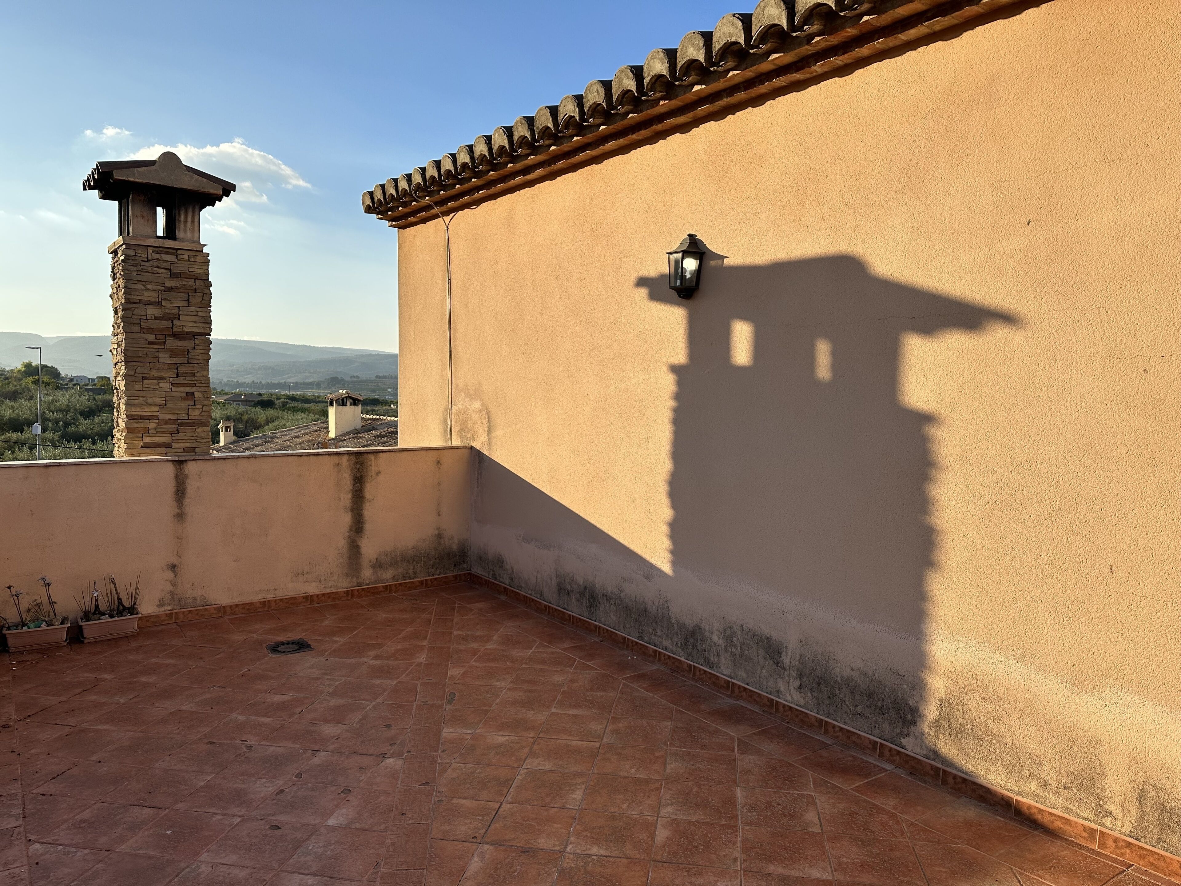 A rooftop terrace with a stone chimney, a wall-mounted light fixture, and terracotta tiles.