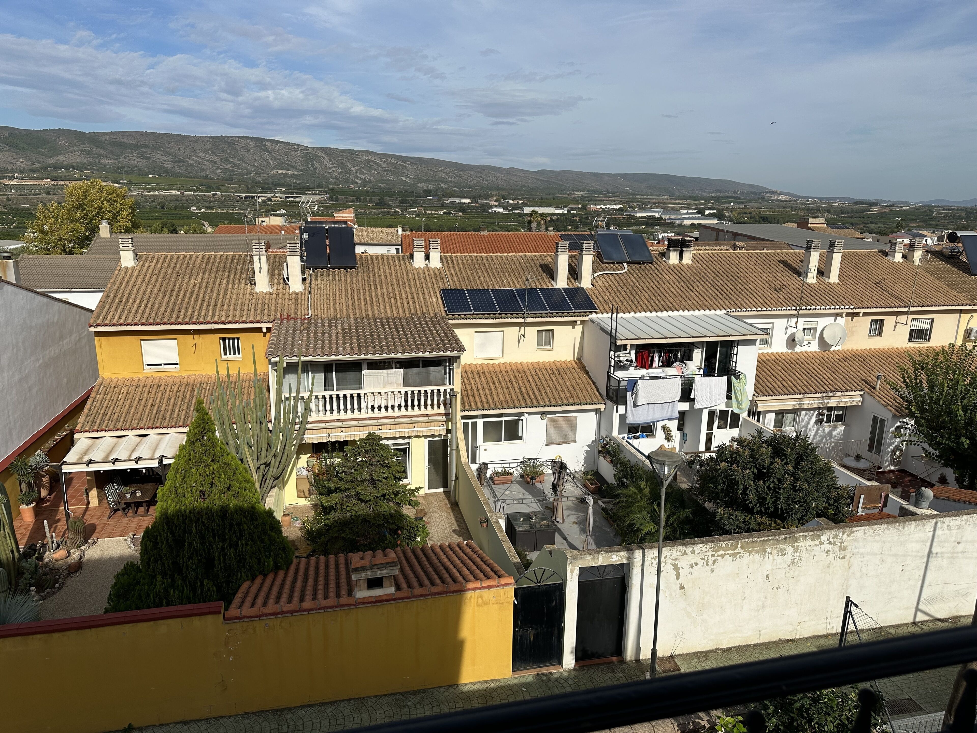 Ein Wohngebiet mit Terrakotta-Dachziegeln, Solaranlagen und Blick auf ferne Hügel.