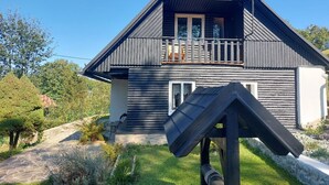 Une maison en bois à deux étages, dotée d’un balcon, d’une antenne parabolique et d’un petit jardin.
