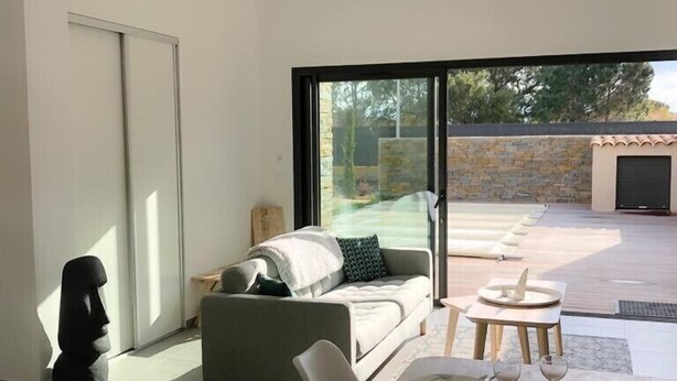 Una sala de estar moderna con un sofá, una mesa de comedor preparada para dos personas y vistas al exterior a través de grandes ventanales.