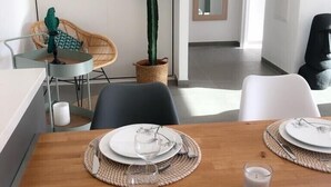 Un comedor con una mesa de madera dispuesta para dos personas, una planta de cactus y una silla de mimbre.