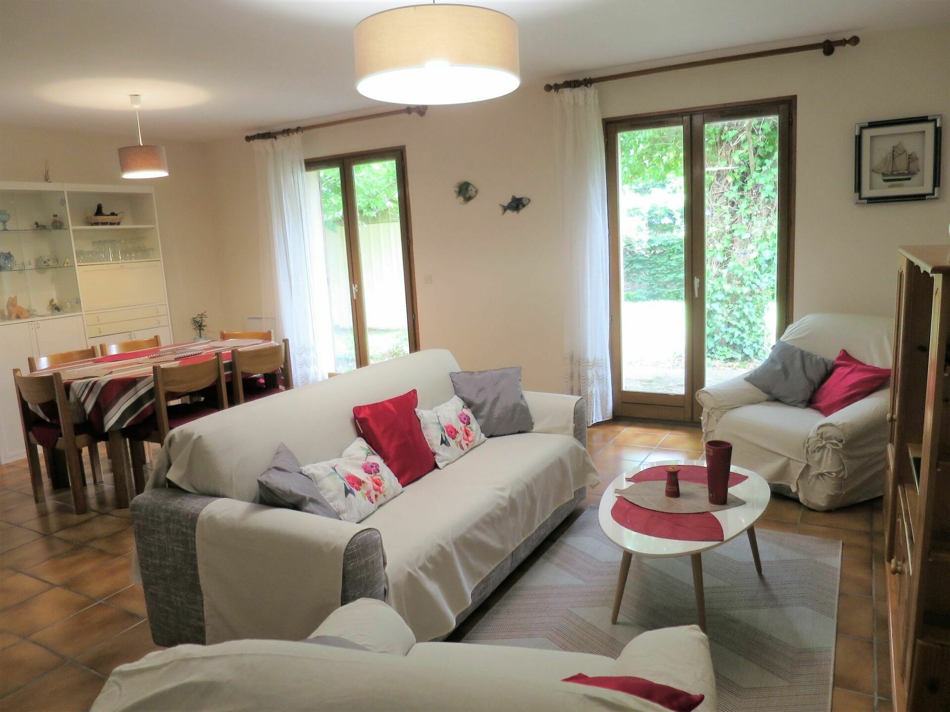 A living room with a sofa, armchairs, a dining table with chairs, and a kitchen area with cabinets and a hanging light fixture.