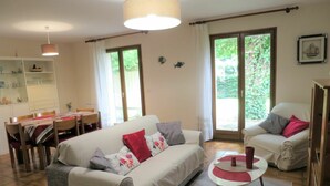 A living room with a sofa, armchairs, a dining table with chairs, and a kitchen area with cabinets and a hanging light fixture. - Stunning private villa for 6 guests with WIFI, TV, terrace and pets allowed (Arès)