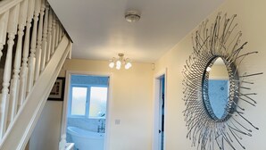 A staircase with white balusters leading to a bathroom with a white bathtub and a wall-mounted mirror with a sunburst design. - Holiday Home Epworth (Doncaster)