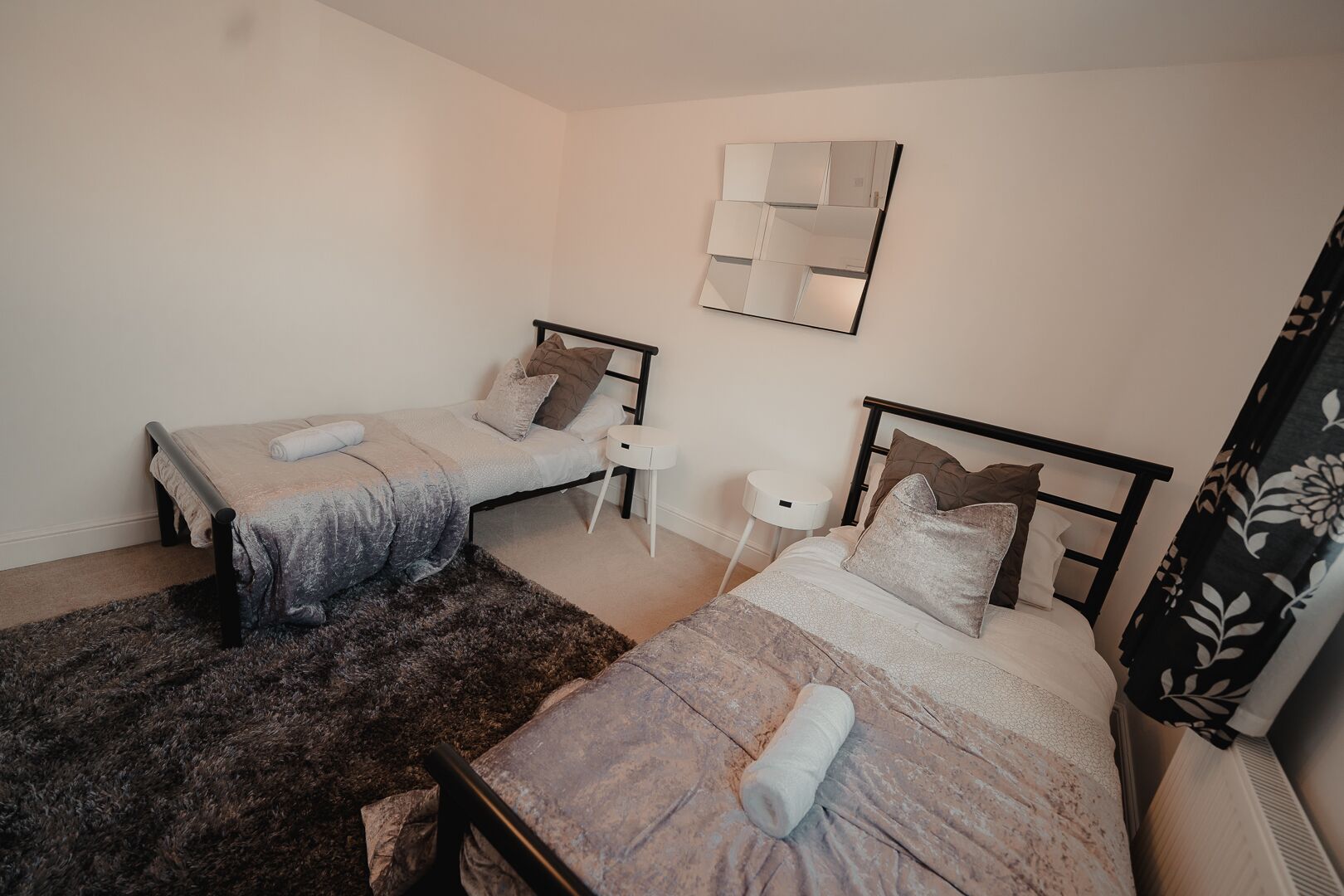 A bedroom with two beds, a small bedside table, a mirror, and a dark rug.