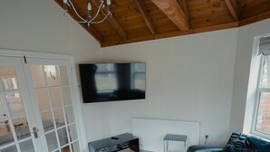 A modern living room with a wooden ceiling, a large flat-screen TV mounted on the wall, a grey sofa, a white furry rug, and a glass coffee table. - Holiday Home Epworth (Doncaster)