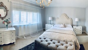 A bedroom with a large bed, two bedside tables with lamps, a dresser, a mirror, and a window with sheer curtains. - Holiday Home Epworth (Doncaster)
