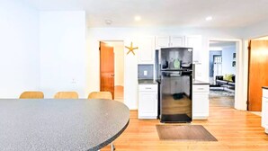 A modern kitchen with white cabinets, a black refrigerator, and a dining area with a round table and chairs. - Discount ! A mile to Narragansett beach & Boon Street Market this home has it all ! (Narragansett)