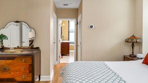 Ein Schlafzimmer mit Bett, Kommode, Spiegel, Lampe und einem Thermostat an der Wand.