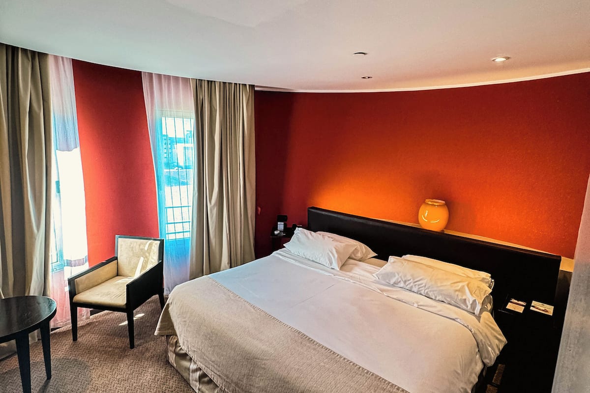 Ein Hotelzimmer mit einem großen Bett, einem Sessel, einem kleinen Tisch und einem Fenster mit Vorhängen.