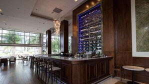 Zona de bar con mostrador de madera, varias opciones de asientos y una amplia estantería para vinos.