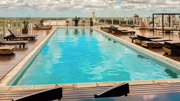 Piscina en la azotea con tumbonas de madera y vistas a la ciudad.