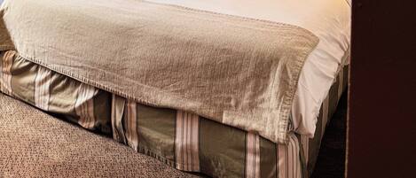 Una habitación de hotel con cama, cortinas, una mesita de noche y una lámpara de pared.