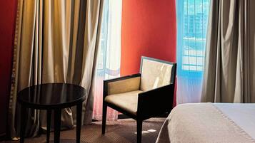 A hotel room with a bed, a chair, a small table, and a window with curtains.
