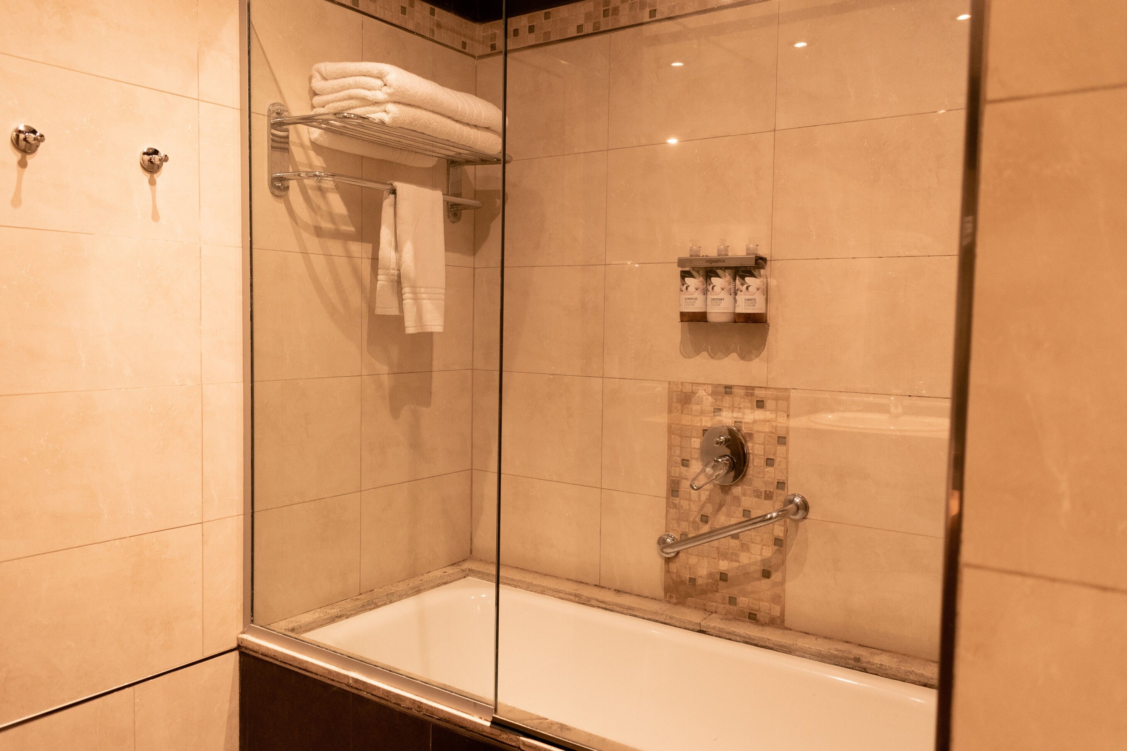 Una ducha moderna con puertas de vidrio, una bañera con cerramiento de vidrio y una pared azulejada con un pequeño estante para artículos de aseo.