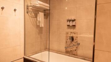 Una ducha moderna con puertas de vidrio, una bañera con cerramiento de vidrio y una pared azulejada con un pequeño estante para artículos de aseo.