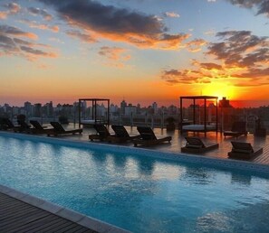 A rooftop pool with lounge chairs and a city skyline at sunset. - Los Silos Hotel (Santa Fe)