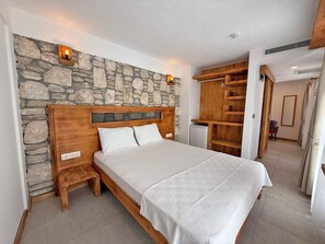 Un dormitorio con pared de piedra, cabecera de madera, mesitas de noche, cama con ropa blanca, armario de madera y un pequeño escritorio.