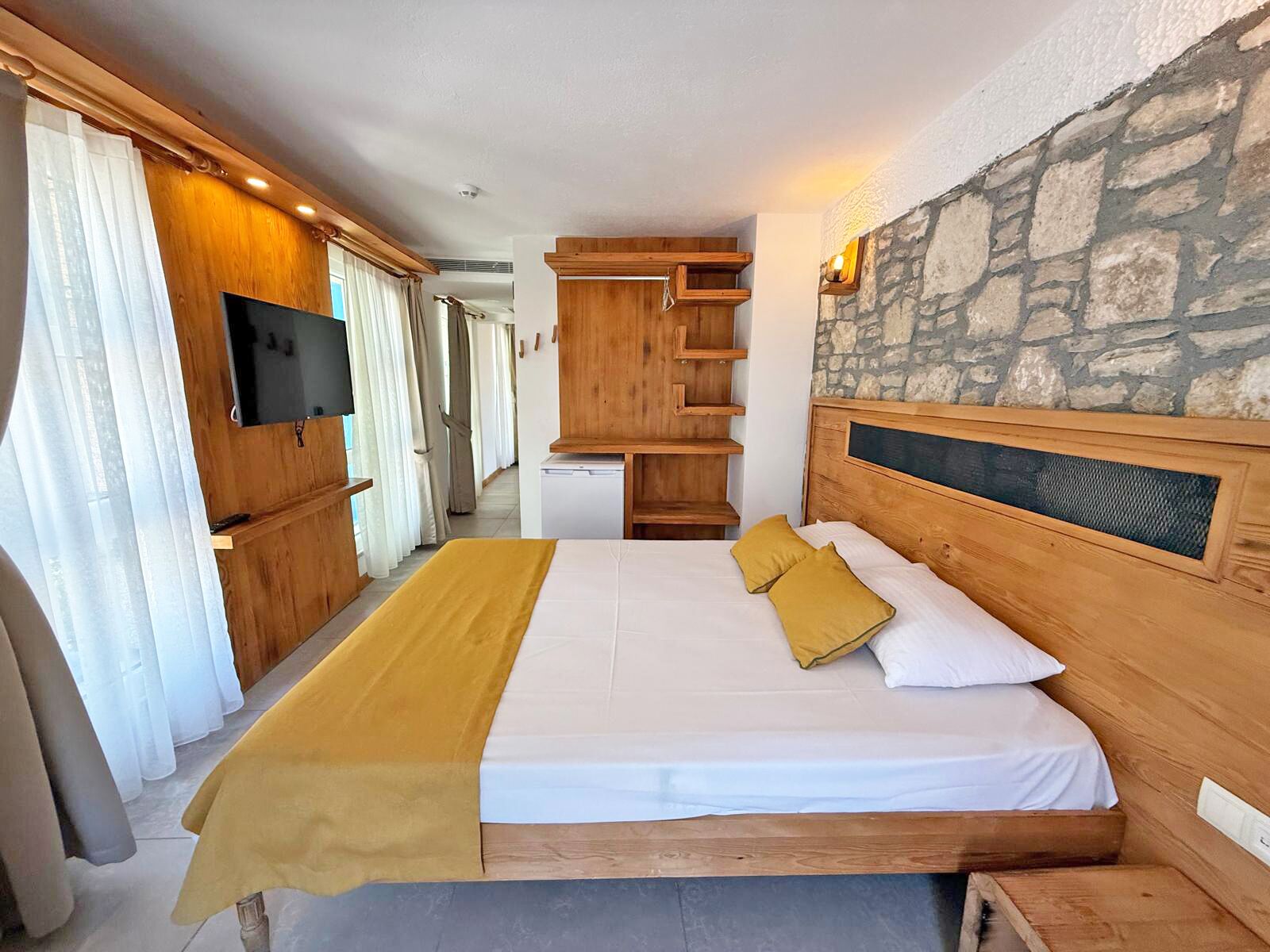 Une chambre à coucher avec un lit, une tête de lit en bois, un mur en pierre et un téléviseur.