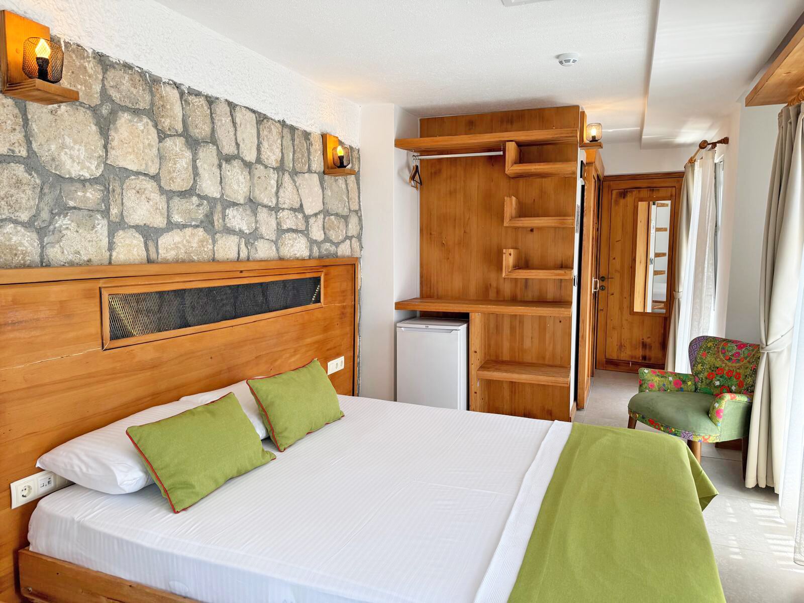 A bedroom with a stone wall, wooden headboard, a bed with green pillows, a desk, and a chair.