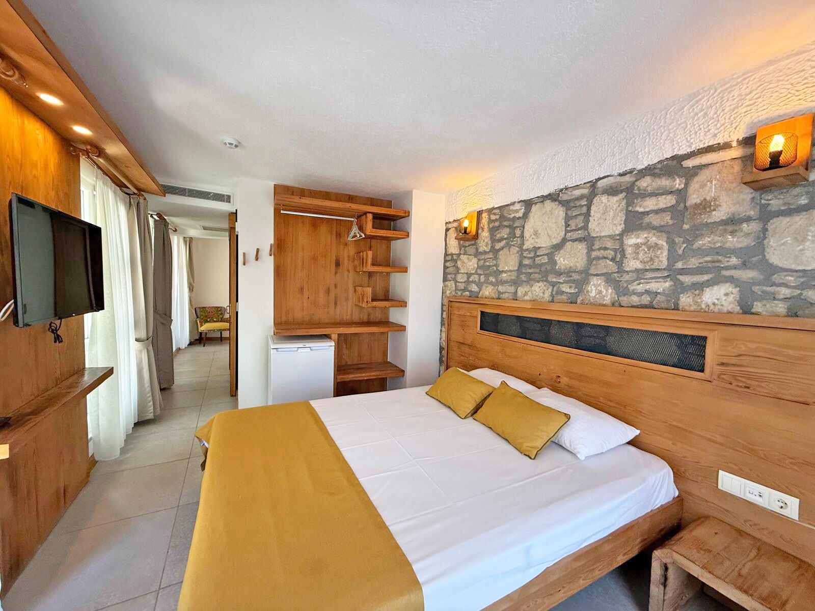 Een slaapkamer met een bed, houten hoofdeinde, stenen muur en een televisie aan de muur.